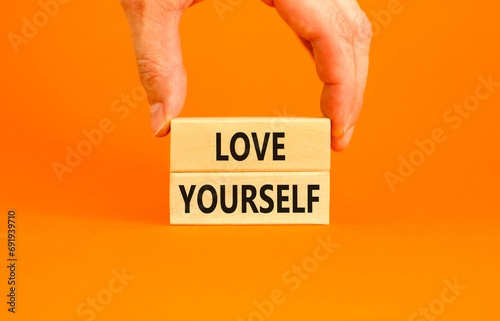 Love yourself symbol. Concept words Love yourself on beautiful wooden blocks. Beautiful orange table orange background. Businessman hand. Psychology love yourself concept. Copy space.
