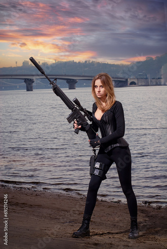 Portrait of young beautiful woman with a assault rifle gun on the river bank