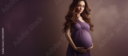 Barely showing young expecting mother wearing a pleated purple dress while forming a heart with her hands over the belly first or second trimester pregnant woman showing love for the baby she c