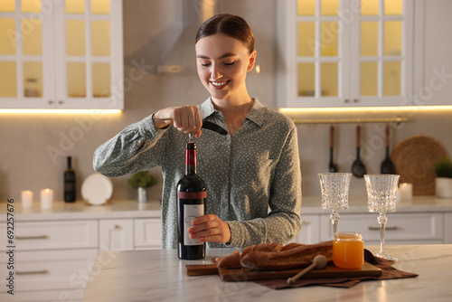 Romantic dinner. Woman opening wine bottle with corkscrew at table in kitchen