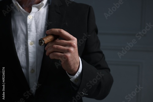 Man smoking cigar on dark grey background, closeup. Space for text