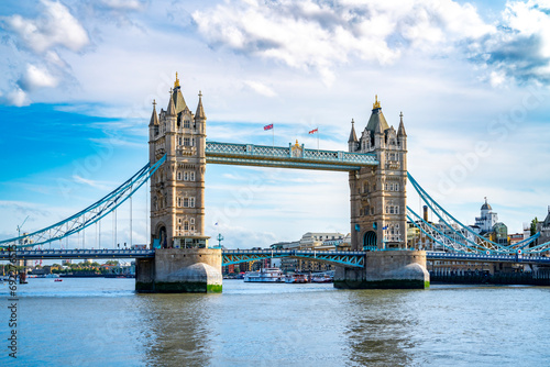 Amazing view of Tower bridge with flags over rippling river against cloudy blue sky in London