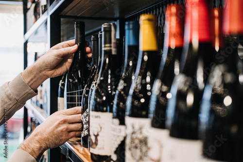 Customer Selecting Wine Bottle from Store Shelf. A person's hand picking a wine bottle from a diverse selection on a well-stocked wine shop shelf
