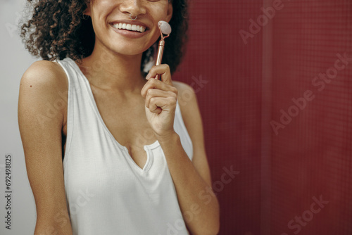 Close up of woman at bathroom use facial roller for skin care in front of mirror. Skin care concept