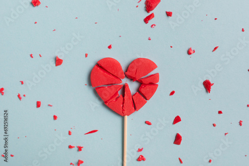 Valentine day concept with broken red lollipop heart on pastel blue background top view. Flat lay greeting card..