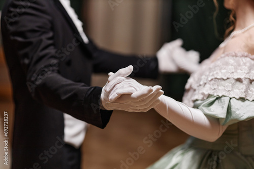 Close up of historical young couple dancing waltz together in ballroom, focus on gloved hands, copy space