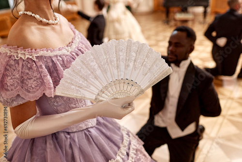 Closeup of beautiful renaissance lady holding fan during ball reception in palace, copy space