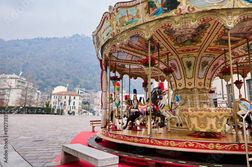 A merry go round, Victorian carousel at Christmas fairground in Como, against Italian Alps backdrop on cloudy winter day
