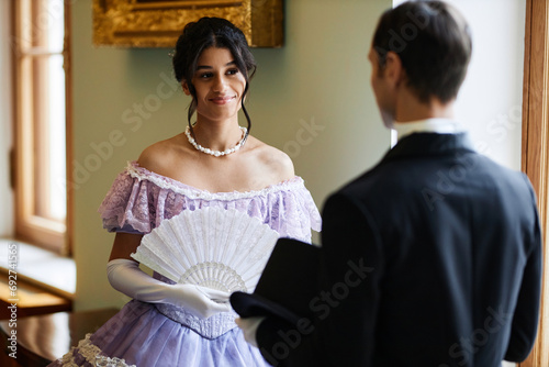 Waist up portrait of elegant young lady talking to gentleman palace hall