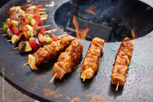 Round grill in the shape of a bowl with fire inside. A man prepares a hearth for barbecue. The round hearth is cleaned before cooking. The firewood lies in the bowl of the outdoor hearth.