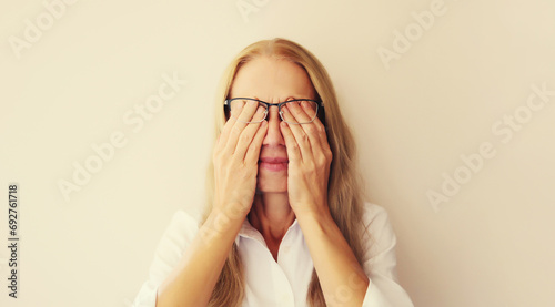Tired overworked middle-aged woman employee rubbing her eyes suffering from eye strain, dry eye syndrome or headaches after working at the computer for a long time. Exhausted office worker