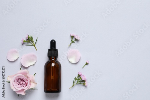 Bottle of cosmetic serum and beautiful flowers on light grey background, flat lay. Space for text