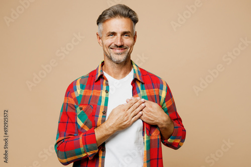 Adult smiling cheerful man wear red shirt white t-shirt casual clothes put folded hands on heart look camera isolated on plain pastel light beige color background studio portrait. Lifestyle concept.