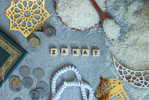 Top view of wooden blocks with Zakat word, rice grain on bowl, rosary beads, money coins. Islamic zakat concept 