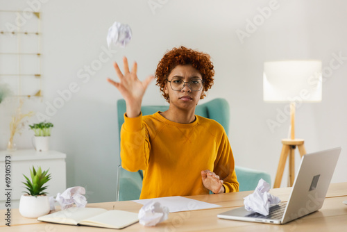 Start up business concept. Sad african business woman writing document crumpled paper and tossed it. Proposed project failed. Tired overworked girl no idea sitting at workplace writing notes at office