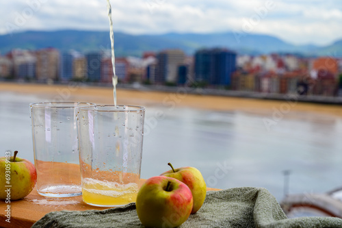 Pouring of natural Asturian cider made from fermented apples in wooden barrels should be poured from great height for air bubbles into the drink and view on San Lorenzo beach of Gijon