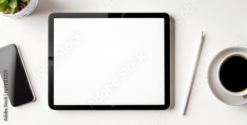 Top view of mockup tablet on white surface with coffee cup, plant cell phone and pen.