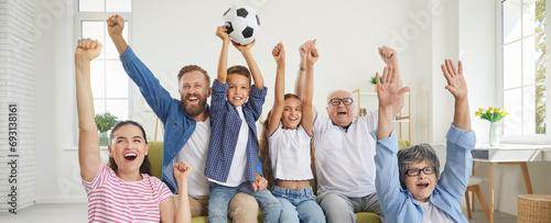 Excited happy family grandparents, parents and children fans watching sport football match on tv supporting their favourite team together sitting on sofa at home with hands up. Banner.