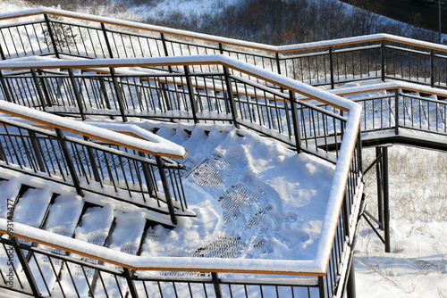 Top view on staircase turns on side of hill at Krasnoyarsk, Russia. Steps of metal staircase and wooden railings covered by fluffy snow