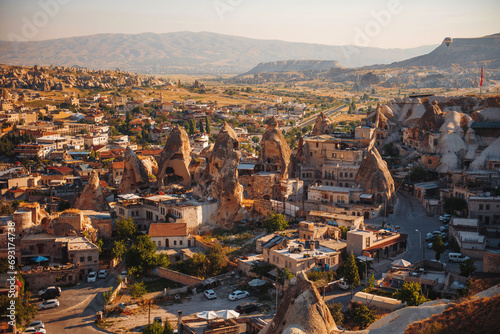 Top view of beautiful small town in Turkey surrounded with rocky mountains. Air Balloons flying in Cappadocia region. Concept of adventure and travelling.