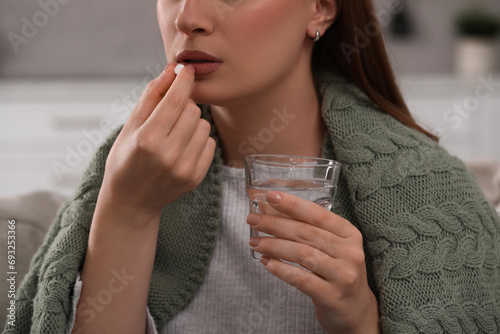 Woman with glass of water taking antidepressant pill on blurred background, closeup