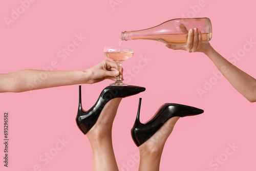 Female legs in high heel shoes with glass and bottle of champagne on pink background. New year party concept