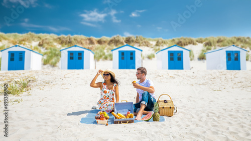 Picnic on the beach Texel Netherlands, couple of men and woman having a picnic on the coast of Texel with white sand and a colorful withe and blue house in Holland