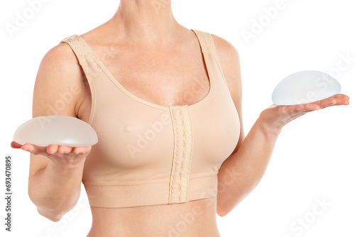 Woman holds round implants wearing compressing bra after breast augmentation.