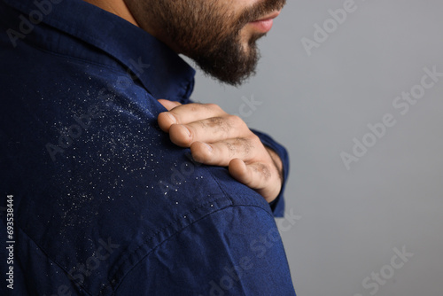 Man brushing dandruff off his shirt on grey background, closeup. Space for text