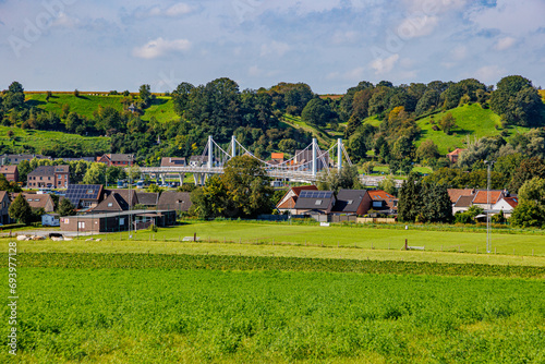 Caestert plateau with green esplanade, suspension bridge, Kanne village and hill with green leaf trees in background, Belgian agricultural land with sown land, sunny day in Riemst, Belgium