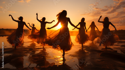 The girls dance in front of the sunset. A group of women dancing on a beach at sunset