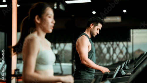 Fit young woman and man running on a treadmill during a workout class at fitness gym