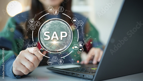 System Applications and Product (SAP). Program helps manage business to access information quickly accurately. Woman using laptop holding magnifying glass with SAP text inside. An icon on background.