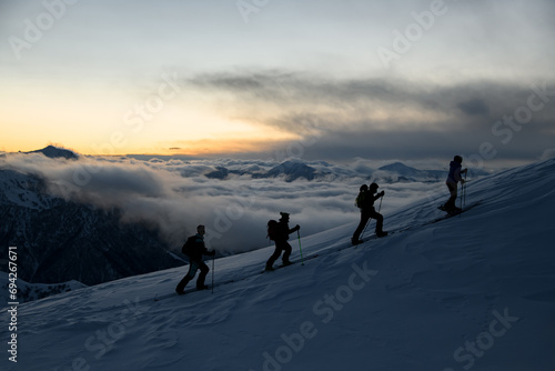 Silhouettes of four skiers with poles walking down the slope