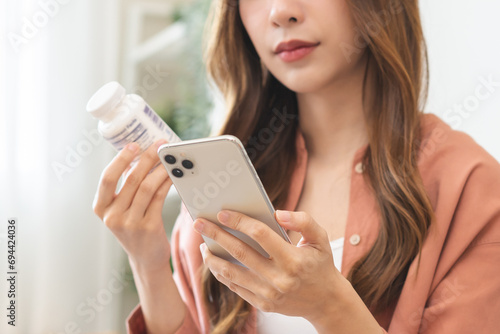Health care asian young woman using smart phone for reading, searching prescription on bottle medicine, pill label text about information online, instructions side effects, pharmacy medicament concept