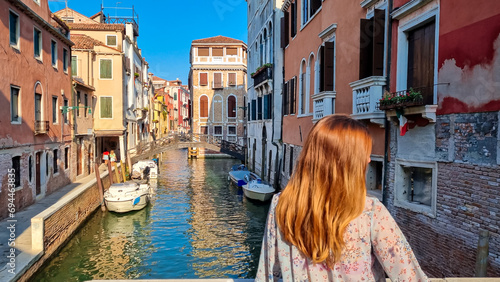 Rear view of woman watching water channel in city Venice, Veneto, Italy, Europe. Venetian architectural landmarks and old houses facades along. Urban tourism in summer atmosphere. Romantic vacation