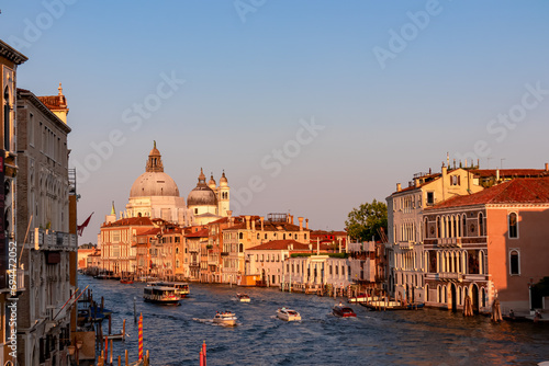 Panoramic sunset view of Grand Canal in city of Venice, Veneto, Italy, Europe. Famous landmark cathedral Santa Maria Della Salute along the water traffic corridor Grand Canale. Urban tourism in summer