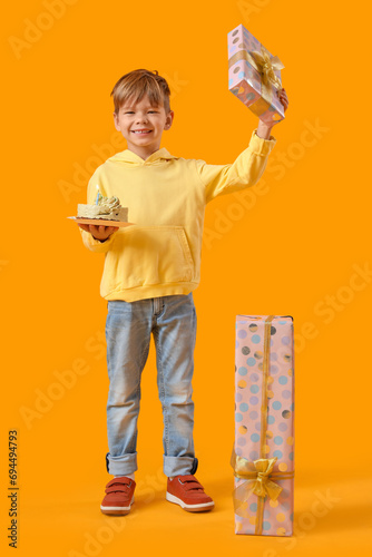 Cute little boy with Birthday cake and gifts on yellow background