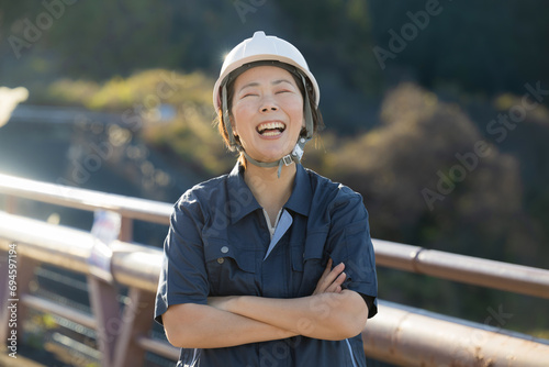 ヘルメットを持つ未来を見つめる中年女性の現場監督の正面、転職や採用のイメージ 半逆光