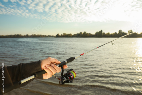 Fisherman with rod fishing at riverside, closeup. Space for text