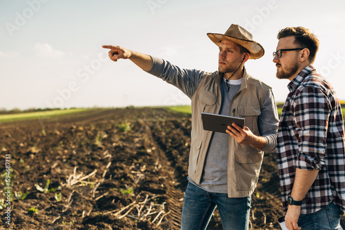 Two man standing in farmland with a tablet and monitoring the field.