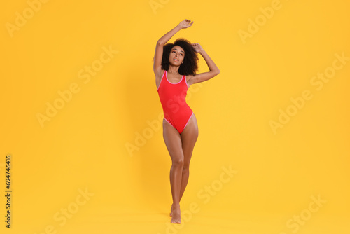 Beautiful woman in bright one-piece summer swimsuit on yellow background