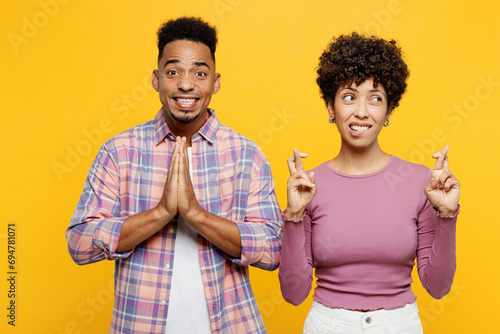 Young couple two friend family man woman of African American ethnicity wear purple casual clothes together hold hands folded in prayer gesture keep fingers crossed isolated on plain yellow background