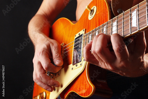 Hands of guitarist playing the orange guitar on dark stage.