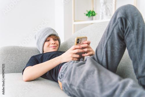young boy lay on the couch at home watching cellphone wearing toque