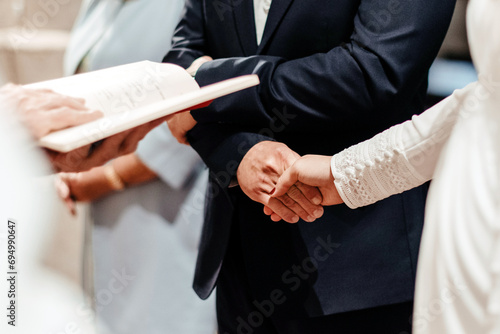 Detalle de una pareja de novios agarrándose de las manos en el altar durante la ceremonia de casamiento frente al sacerdote. Concepto del sacramento del matrimonio en la iglesia Católica