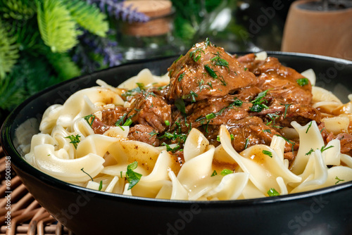 Pasta with beef stew in black bowl.