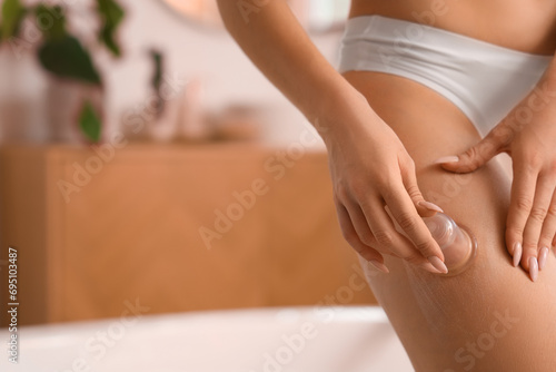 Young woman massaging her thigh with anti-cellulite cup in bathroom, closeup