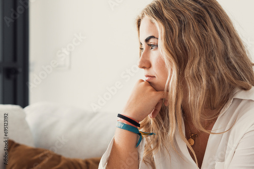 Side view young woman looking away at window sitting on couch at home. Frustrated confused female feels unhappy problem in personal life quarrel break up with boyfriend or unexpected pregnancy concept