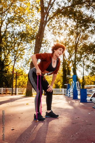 Adult Caucasian woman does stretching with elastic band on street. Healthy lifestyle and training in park. Vertical orientation